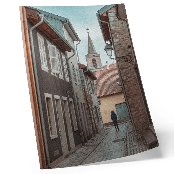 Poster narrow street with tenement houses, a tower, and a figure in a blue coat