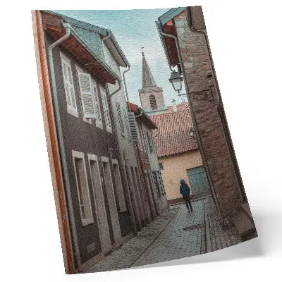 Poster narrow street with tenement houses, a tower, and a figure in a blue coat
